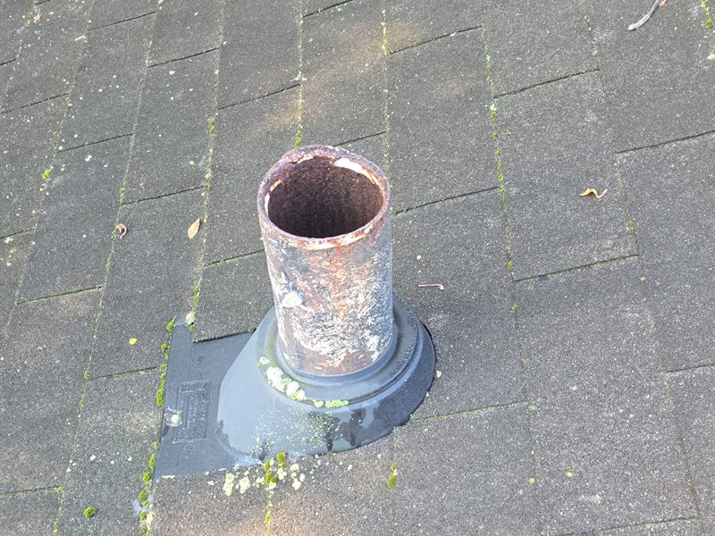 A plumbing vent pipe boot whose rubber collar has hardened and pulled away from the pipe, with moss on the shingles around it.