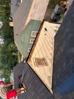 A crew on a steep gable roof tearing off old shingles, with bare wood decking exposed on the upper slope and the remaining old shingles below.