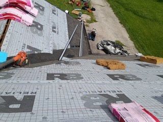 A roof slope covered in gray synthetic underlayment, with bundles of new shingles staged along the ridge and a run of ice-and-water membrane visible in the valley.