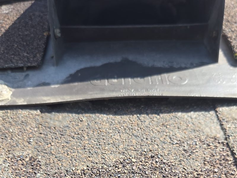 A metal roof vent whose base flange sits on top of the shingles, sealed with a wide smear of grey sealant that has dried and cracked along the lower edge.